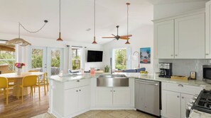 A modern kitchen with white cabinetry, a built-in dishwasher, a stove, and a dining area with yellow chairs and a table. - Sleeps 18! 2 Homes, Hot Tub, Game Room, Walk to the Beach Haven & Hidden Grove (St. Augustine)