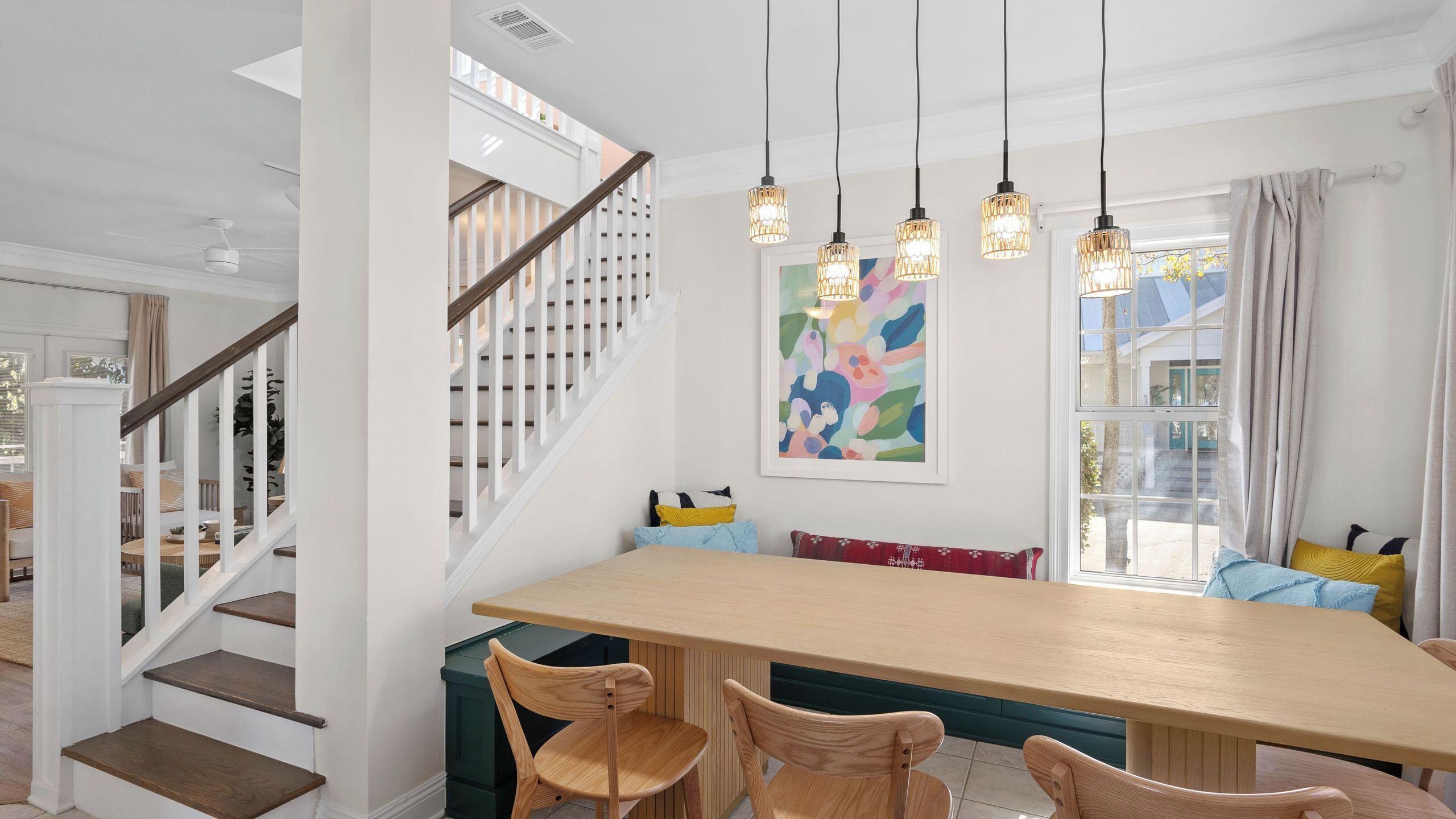 Un espace repas comprenant une table en bois, des chaises, un escalier et un tableau abstrait aux couleurs vives.