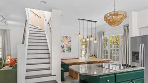 Une cuisine moderne dotée d’un îlot central, d’un escalier menant à un autre niveau et d’un coin repas offrant une vue sur l’extérieur.