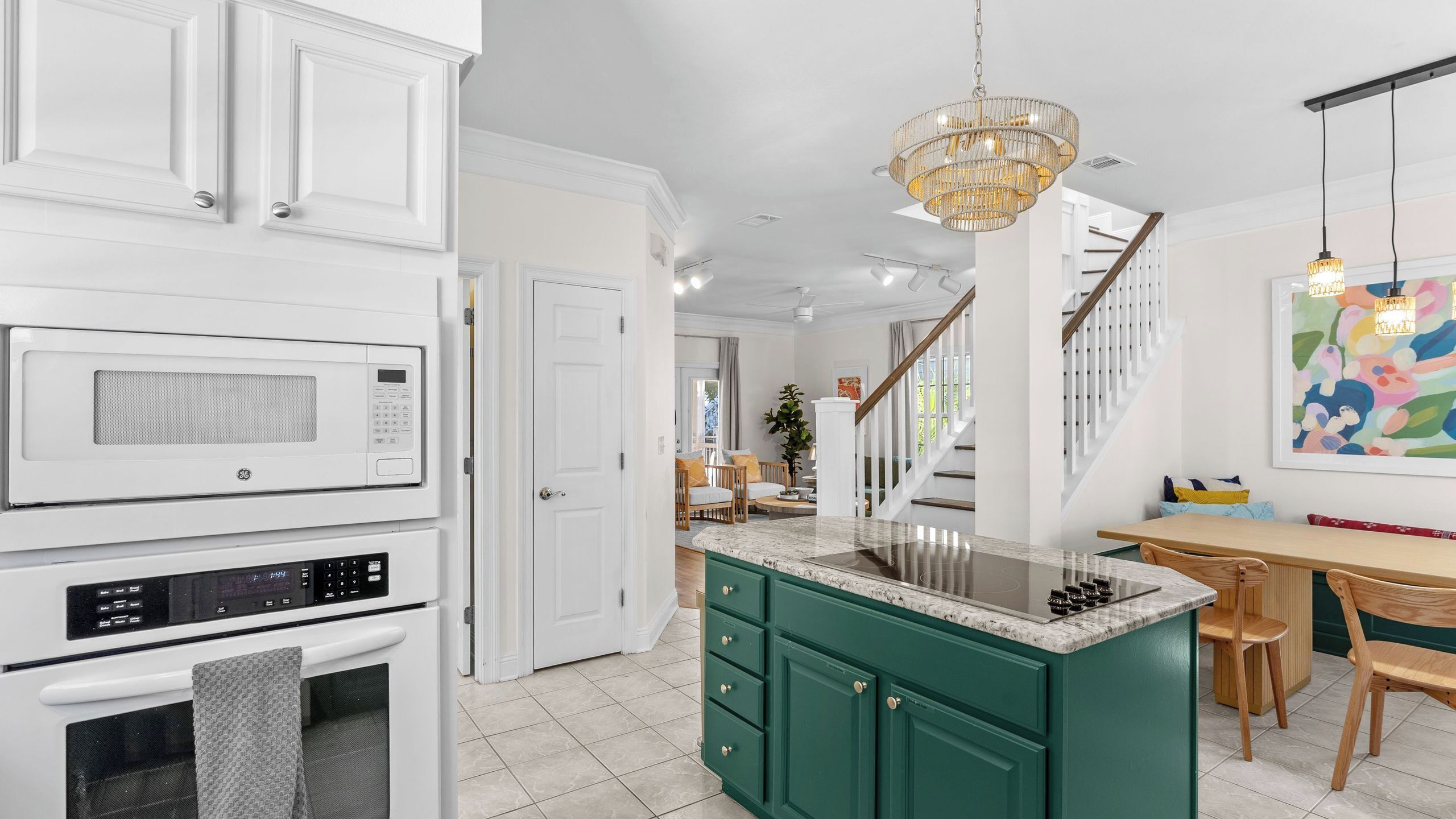 A kitchen with white cabinetry, a green island, a stainless steel sink, and a chandelier.