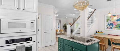 A kitchen with white cabinetry, a green island, a stainless steel sink, and a chandelier.