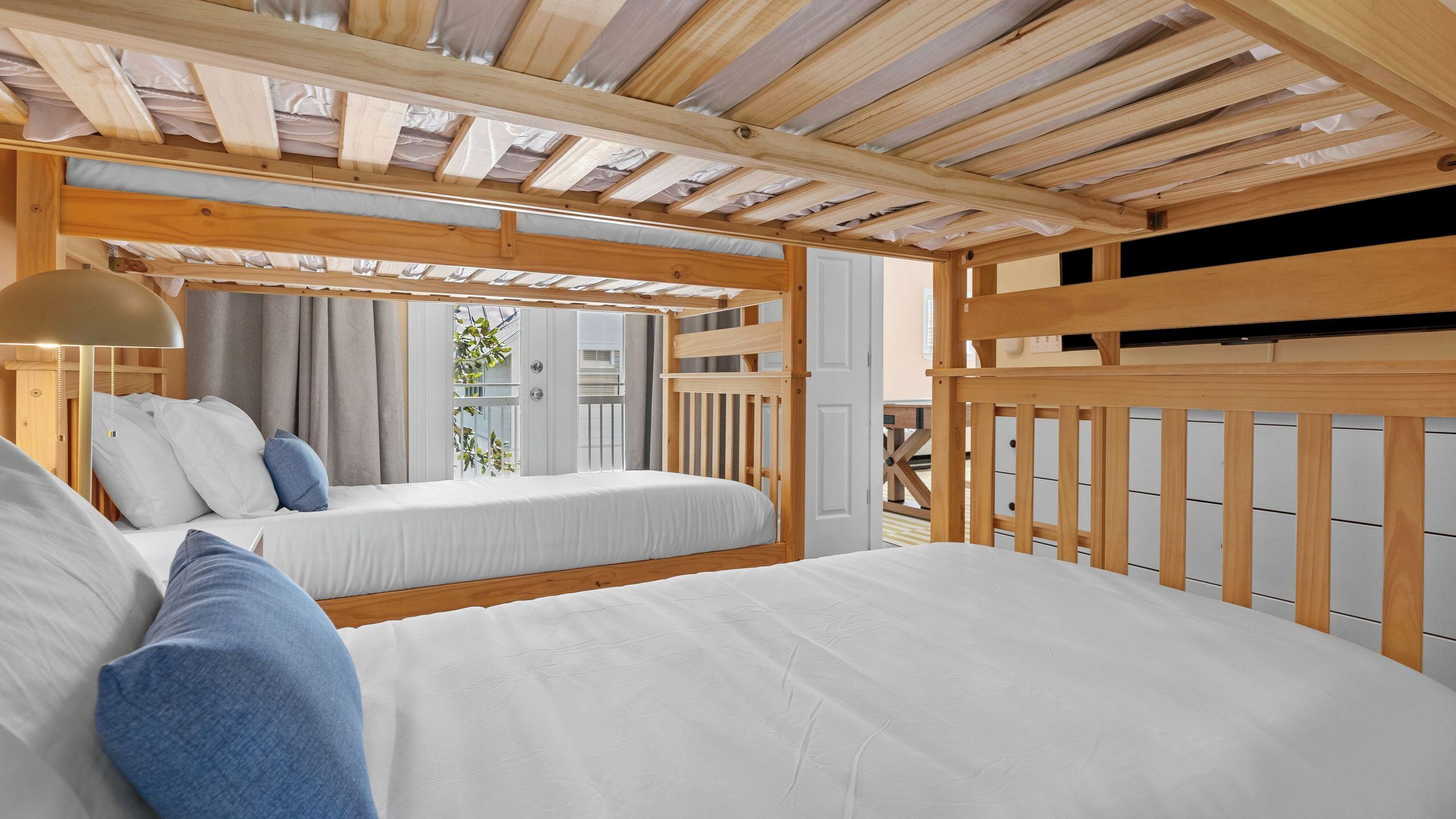 A bedroom with two beds, wooden headboards, a ceiling with wooden beams, and a window with curtains.