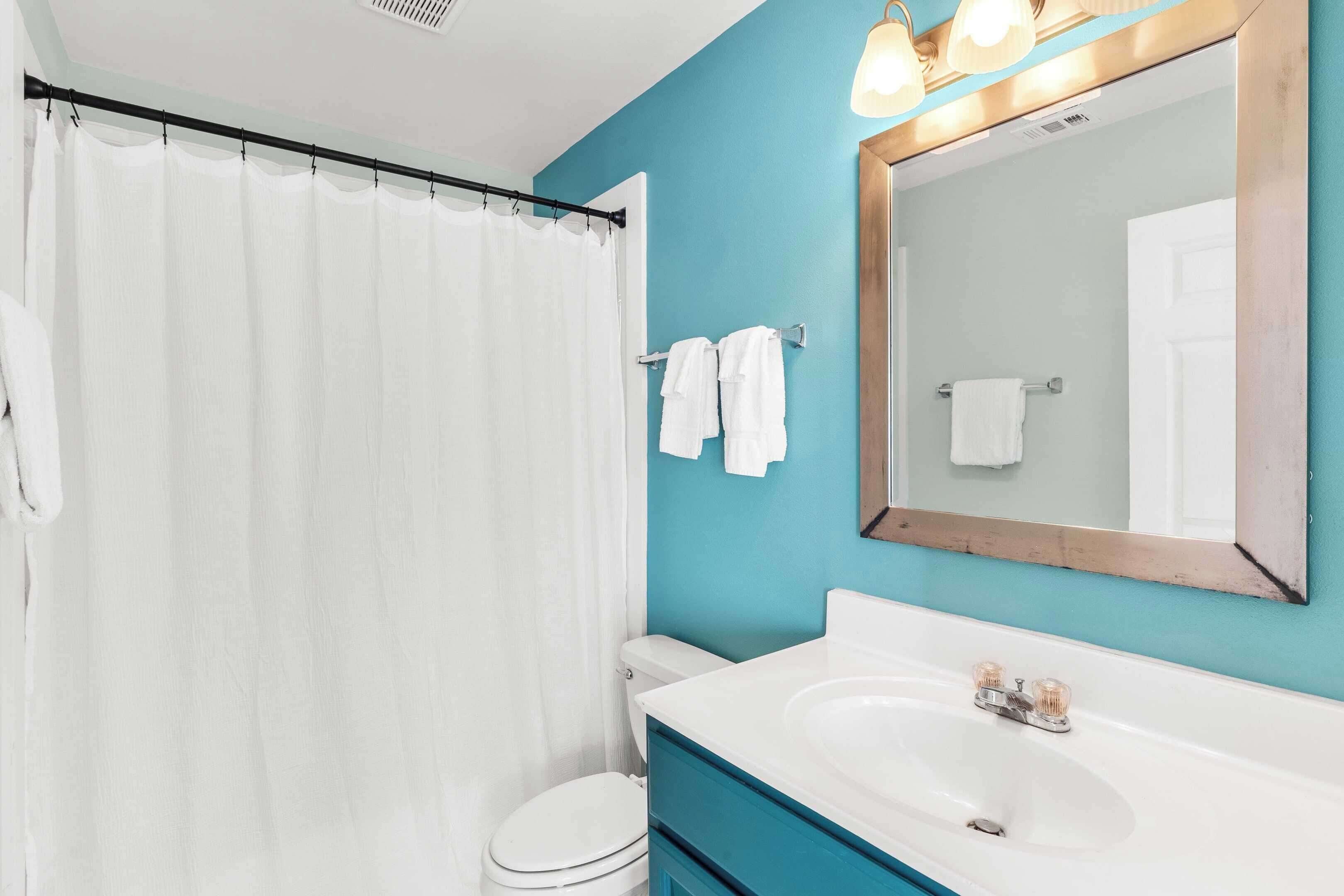 Une salle de bain avec des toilettes blanches, un lavabo blanc et un rideau de douche.