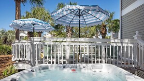 Un bain à remous agrémenté de deux parasols à rayures, entouré d’une terrasse blanche et de palmiers.