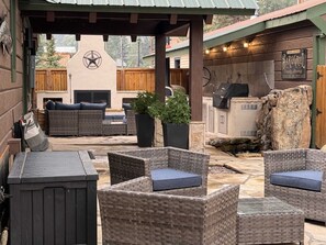 An outdoor patio with wicker furniture, a barbecue grill, and a stone fireplace.