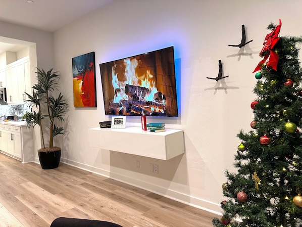 A modern living room with a flat-screen TV, a fireplace, a Christmas tree, and a potted plant.