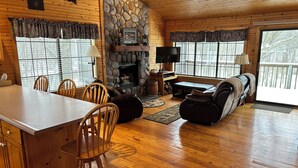 Un interior de cabaña acogedor, con chimenea de piedra, muebles de madera y ventanas amplias.