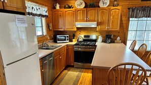 Una cocina con armarios de madera, electrodomésticos de acero inoxidable, microondas, estufa, lavabo y una zona de comedor con sillas de madera.