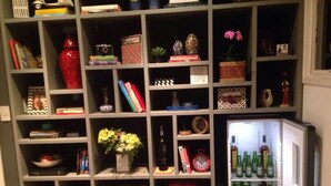 A compact living space with a built-in bookshelf, a small refrigerator, and various decorative items. - Spacious, modern and cozy apartment very well located (Itaim Bibi São Paulo)