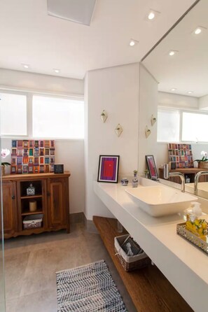 A modern bathroom with a large mirror, a wooden cabinet, and a built-in sink. - Spacious, modern, and cozy apartment in a great location (Itaim Bibi São Paulo)