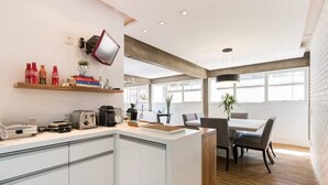 A modern kitchen with white cabinets, a wooden countertop, and a dining area with a table and chairs. - Spacious, modern and cozy apartment very well located (Itaim Bibi São Paulo)
