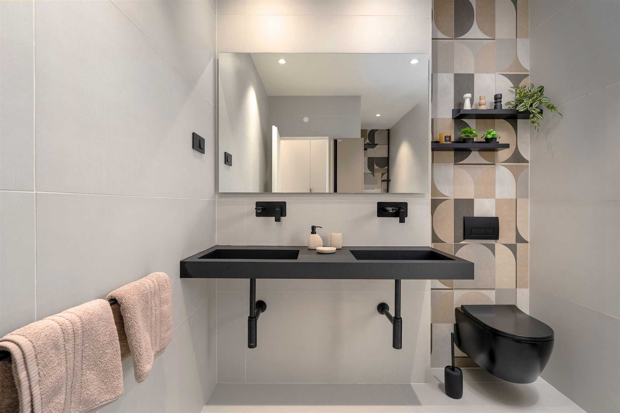 Un baño moderno con un lavamanos negro, un perchero para toallas, un inodoro y un espejo.