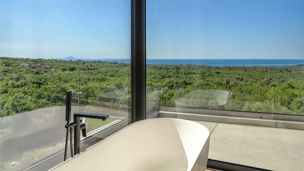 A balcony with a clear view of a coastal landscape, including a road and distant buildings.