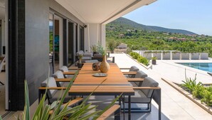 A modern outdoor dining area with a pool and a scenic mountain view.