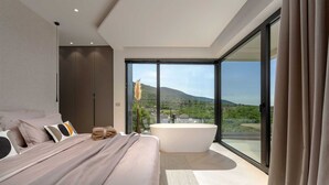 A modern bedroom with a large bed, a bathtub, and a view of a mountainous landscape.