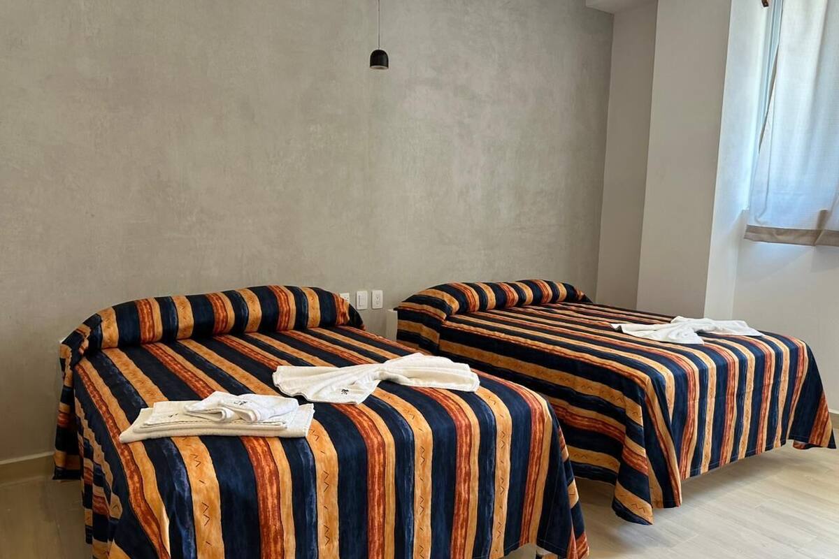 Dos camas individuales con ropa de cama a rayas, una lámpara colgante y una ventana con cortinas.