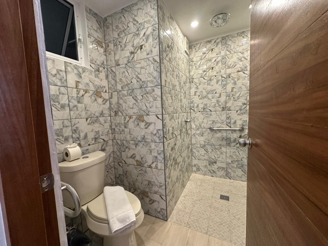 Un baño con inodoro, ducha y paredes con diseño de mármol.
