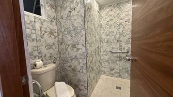 Un baño con inodoro, ducha y paredes con diseño de mármol.