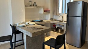 Eine kompakte Küche mit einer Kücheninsel aus Granit, einem Edelstahlkühlschrank und einem Fenster mit Vorhängen.