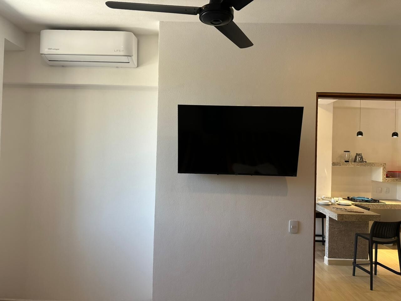 Sala de estar con televisor montado, ventilador de techo y aire acondicionado.