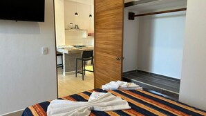 Ein Hotelzimmer mit Bett, einer Holztür, einer kleinen Küchenzeile und Blick auf das angrenzende Zimmer.