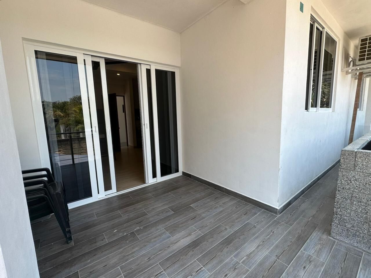 Una habitación con puerta corrediza de vidrio que da a un balcón, piso de baldosas y un pequeño espacio de descanso.