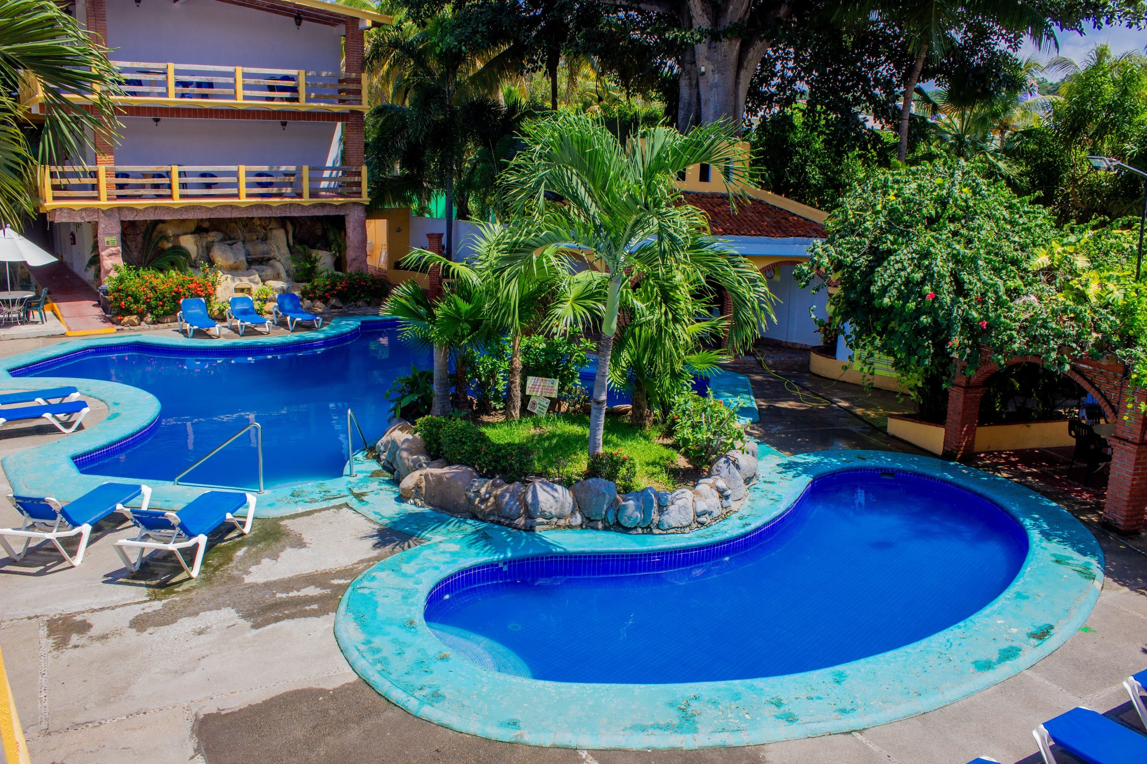 Un área de piscina con varias piscinas azules, rodeada de palmeras y tumbonas.