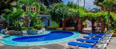A swimming pool with blue tiles, surrounded by lounge chairs and palm trees.