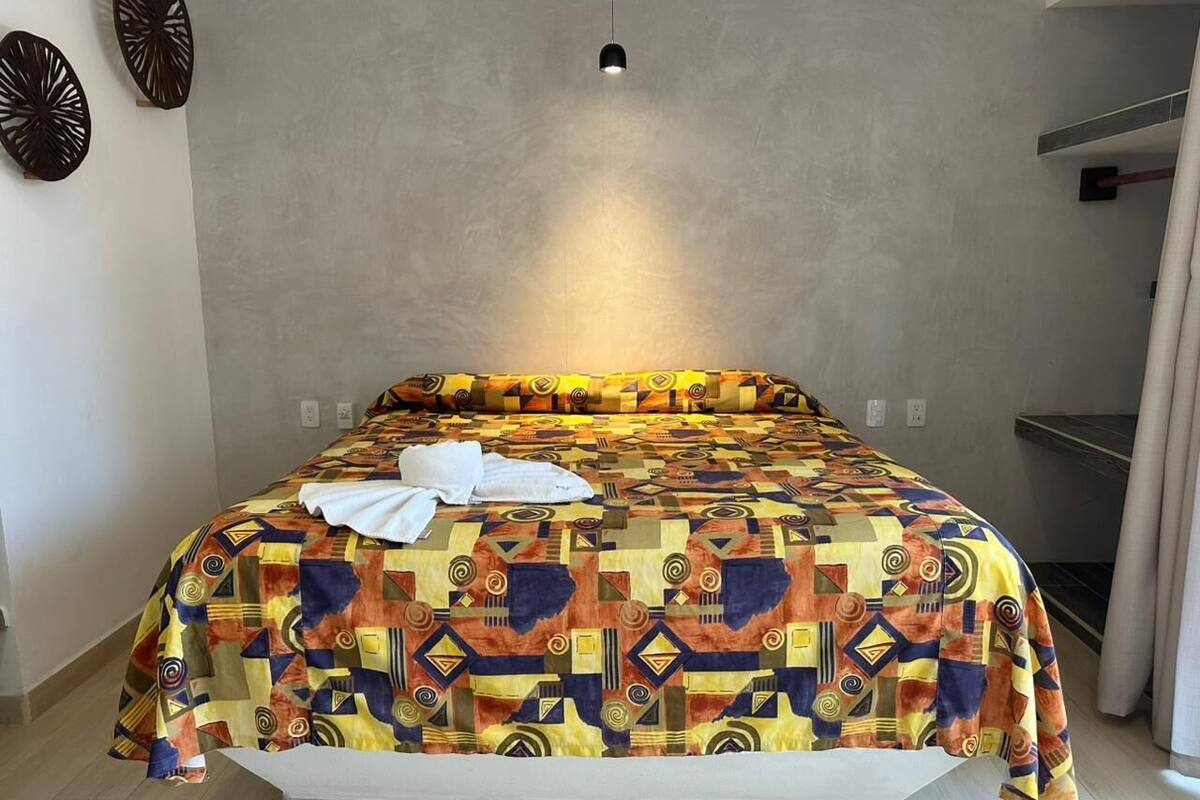 Una cama con una colcha estampada, una toalla blanca encima y una lámpara colgante por arriba.