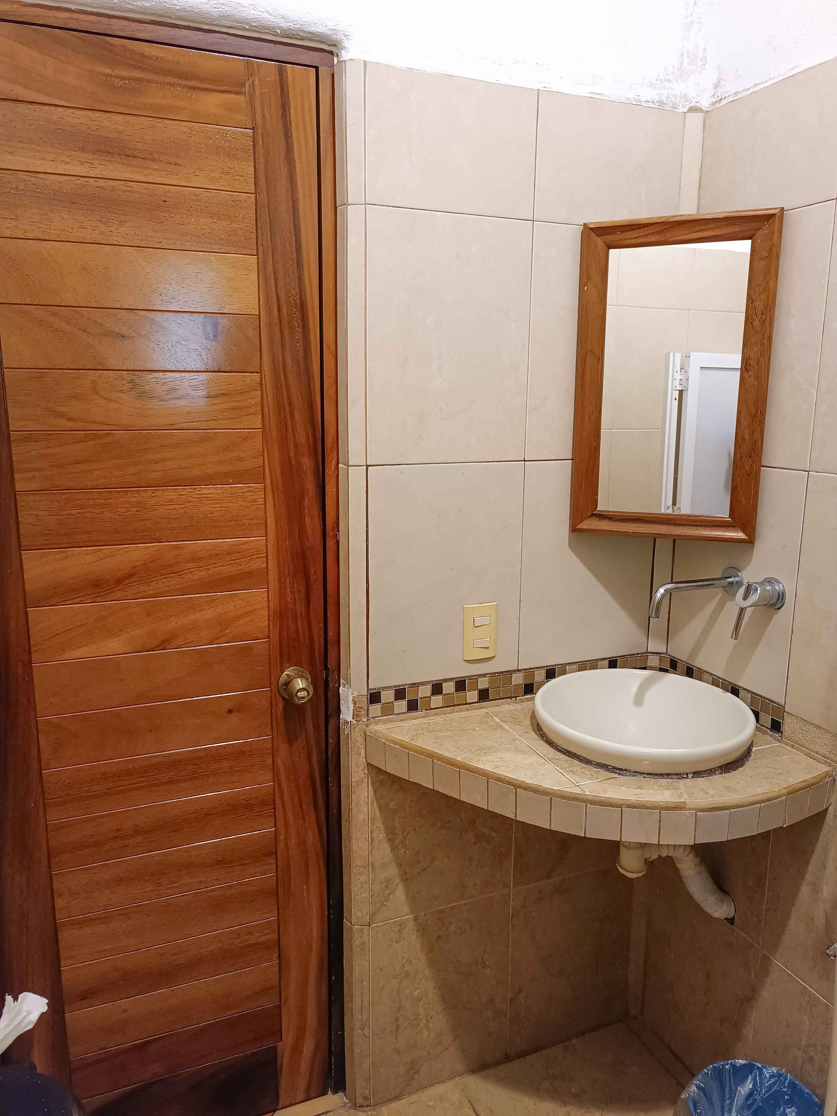Un baño con puerta de madera, un lavabo con espejo y paredes de azulejos.