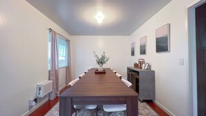 Une salle de conférence avec une longue table, des chaises blanches, un vase avec des plantes et des tableaux encadrés accrochés au mur.