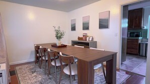 Un coin repas avec une table en bois et six chaises, une petite plante et trois tableaux encadrés accrochés au mur.