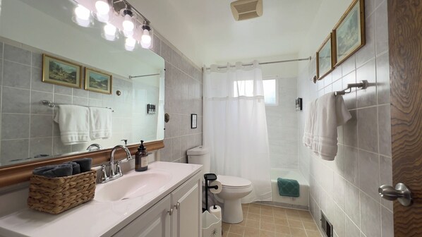 Een badkamer met een grote spiegel, een wastafel met een mand handdoeken, een toilet en een douchehoek.