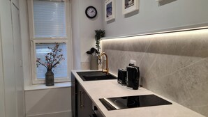 Una cocina moderna con estufa integrada, una ventana con persianas, un reloj y una pequeña planta en el alféizar.