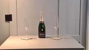 Una mesa con dos sillas, una botella de champán y dos copas sobre una superficie blanca.