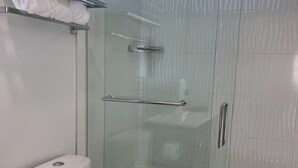 A modern bathroom with a glass-enclosed shower, a toilet, and a shelf with neatly folded towels. - MoonBeam: Spacious and Modern Home in the countryside near Stockton Lake.  (Stockton)