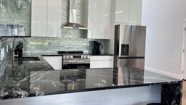 A modern kitchen with a marble countertop, stainless steel appliances, and a backsplash with a textured pattern. - MoonBeam: Spacious and Modern Home in the countryside near Stockton Lake.  (Stockton)
