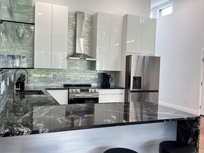 A modern kitchen with a marble countertop, stainless steel appliances, and a backsplash with a textured pattern. - MoonBeam: Spacious and Modern Home in the countryside near Stockton Lake.  (Stockton)