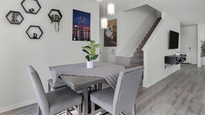 Een moderne woonkamer met een eethoek, met een trap, een flatscreen-tv en een wandkunst met een honingraatpatroon.