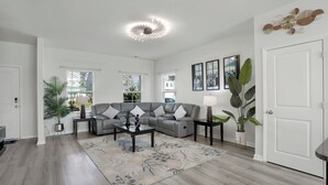Een moderne woonkamer met een grijze bank, een salontafel en een grote plant.