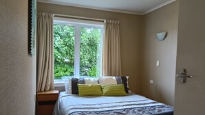 Een slaapkamer met een bed, een raam met gordijnen, een nachtkastje en een wandlamp.