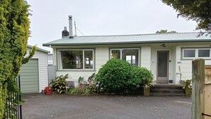 Een gelijkvloers huis met een voordeur, een garagepoort en een kleine voortuin met verschillende planten en een tuinslang.