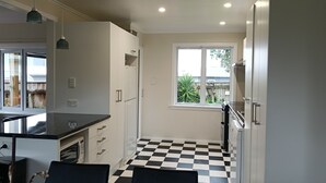 Een compacte keuken met een zwart-wit schakerend vloertje, witte kasten en een raam met uitzicht op de achtertuin.