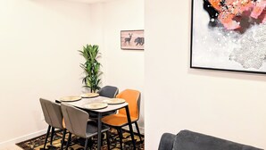 A modern living room with a dining area, featuring a black sofa, a patterned rug, and a large abstract painting. - Luxury and Modern 2 bedroom suite (Balzac)