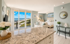 A room with a large sliding glass door leading to a balcony with a view of the beach.