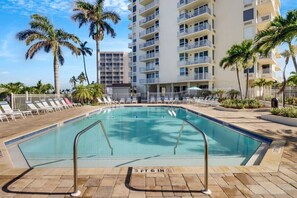 A swimming pool with a 3 FT 6 IN depth marker, surrounded by lounge chairs and palm trees, with a multi-story building in the background.
