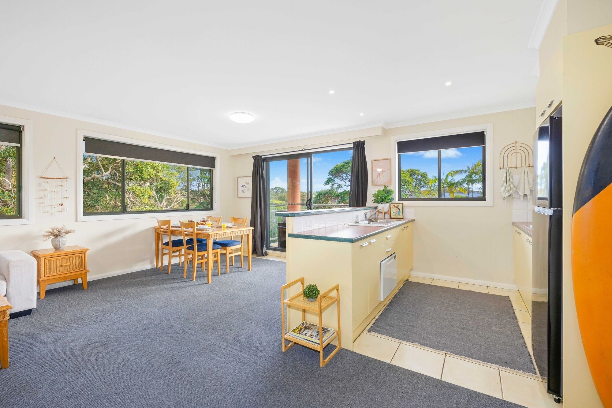 A modern kitchen with a dining area, large windows, and a view of trees.