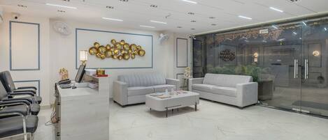 Una moderna zona de recepción con suelo de mármol, dos sofás, un mostrador de recepción y una puerta de cristal que da al exterior.