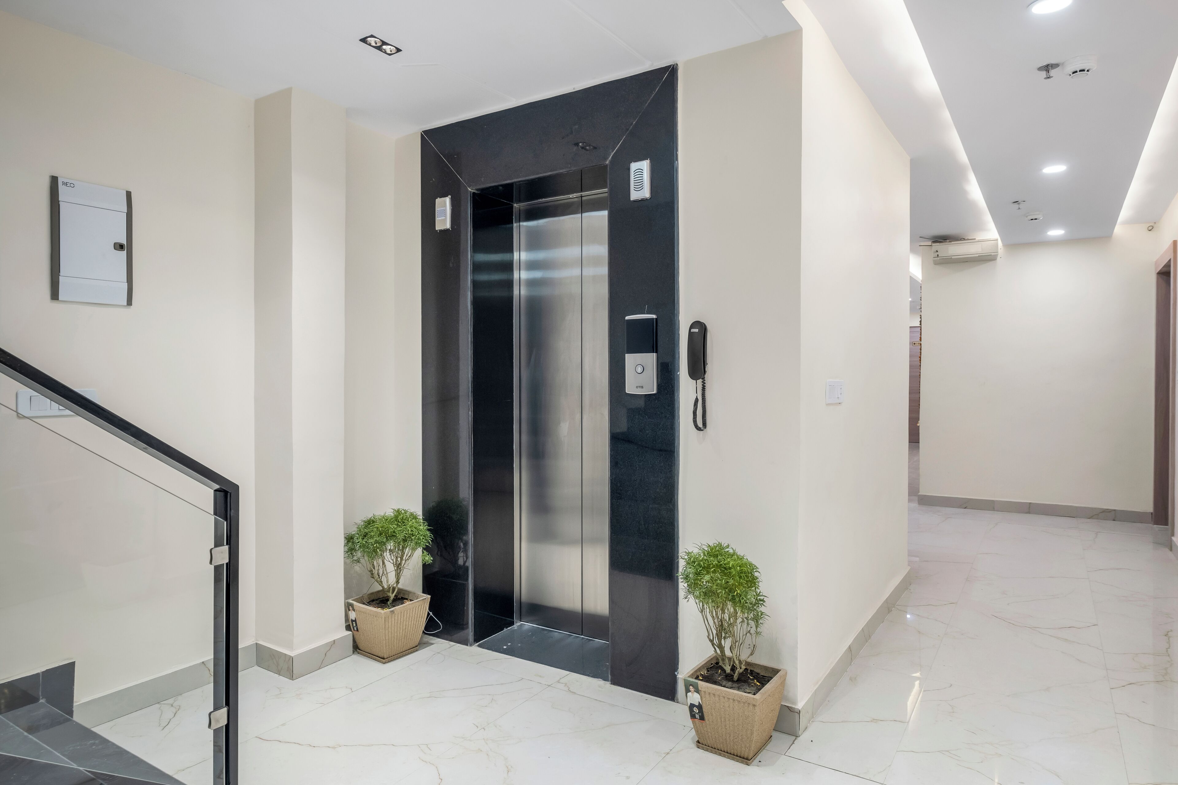 A modern elevator with a phone, a wall-mounted intercom, and potted plants.