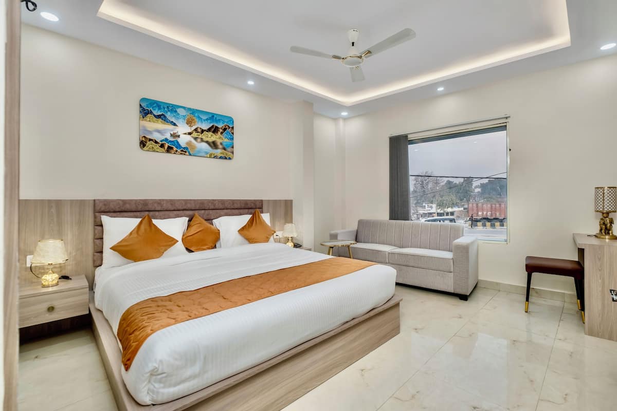 Quarto de hotel moderno com cama grande, sofá, escrivaninha e janela com vista para a cidade.
